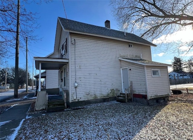 rear view of house featuring a porch, entry steps, roof with shingles, and a chimney