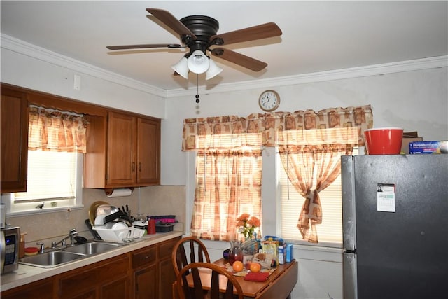 kitchen with brown cabinets, freestanding refrigerator, light countertops, crown molding, and a sink