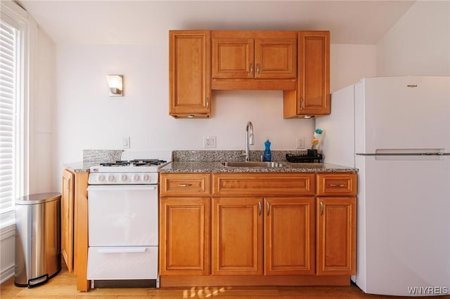 kitchen with light stone counters, white appliances, brown cabinetry, and a sink