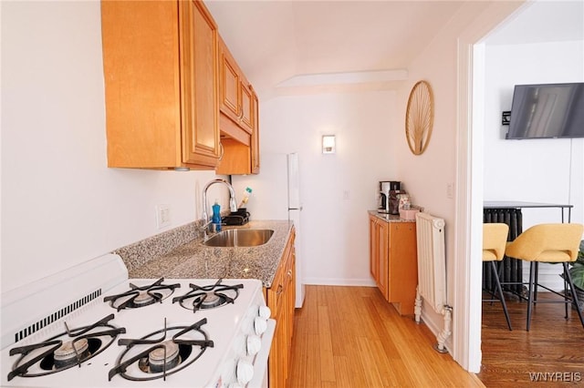 kitchen with light stone counters, white gas stove, light wood finished floors, radiator, and a sink