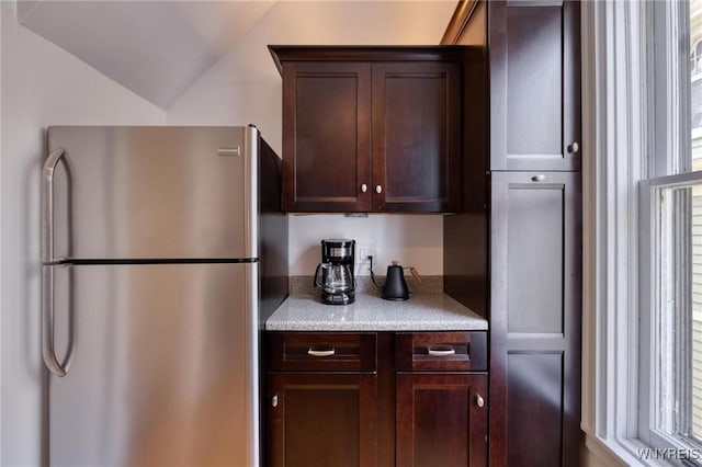 kitchen with lofted ceiling, dark brown cabinetry, light countertops, and freestanding refrigerator