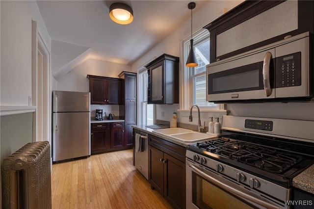 kitchen with radiator heating unit, appliances with stainless steel finishes, light wood-style floors, pendant lighting, and a sink