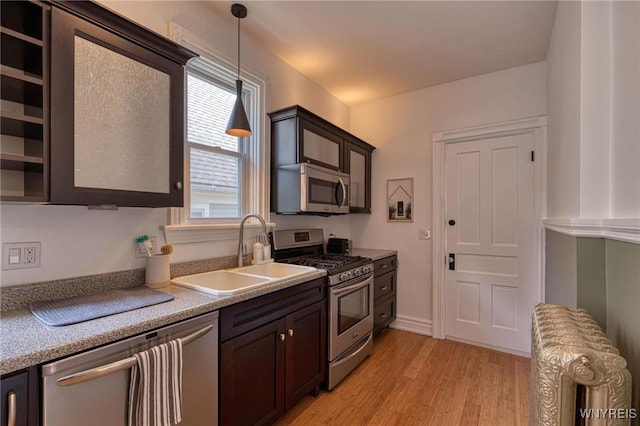 kitchen featuring light wood-style flooring, dark brown cabinetry, stainless steel appliances, a sink, and decorative light fixtures