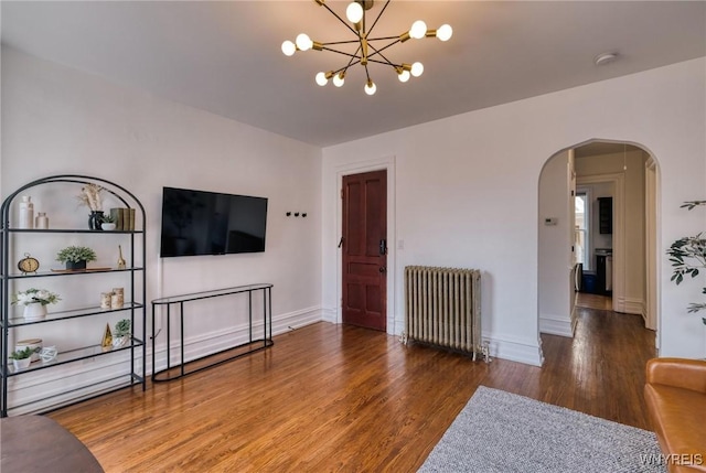 living area with baseboards, arched walkways, radiator heating unit, wood finished floors, and a notable chandelier