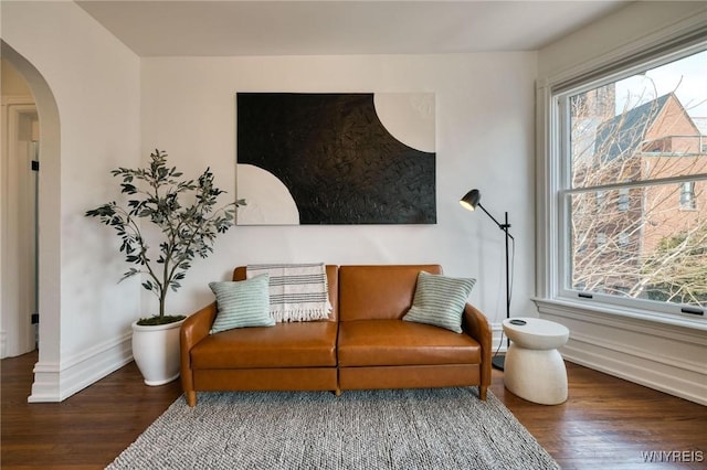 living area with baseboards, arched walkways, and wood finished floors