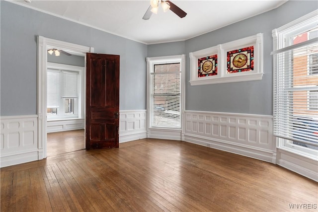 empty room with a wainscoted wall, ceiling fan, ornamental molding, and wood finished floors