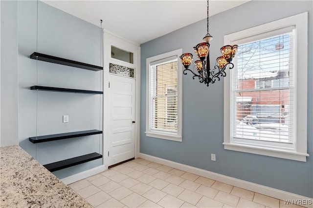 unfurnished dining area with plenty of natural light, baseboards, and an inviting chandelier