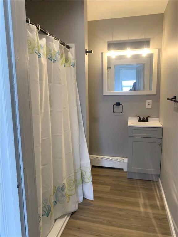 full bathroom with a shower with shower curtain, vanity, wood finished floors, baseboards, and a baseboard heating unit