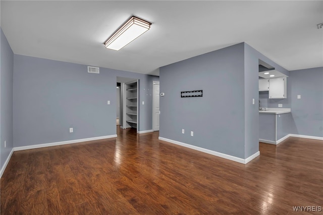 empty room featuring dark wood-style flooring, visible vents, and baseboards