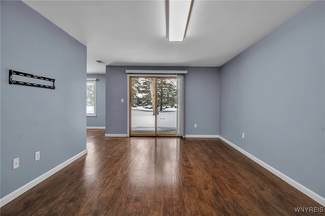 empty room with dark wood-style flooring, visible vents, and baseboards