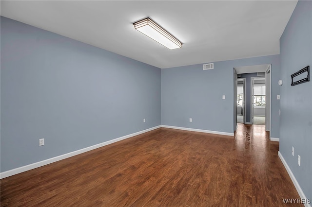 empty room with dark wood-style floors, baseboards, and visible vents