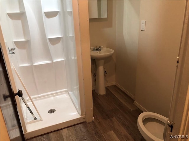 full bathroom featuring a stall shower, baseboards, toilet, wood finished floors, and a sink