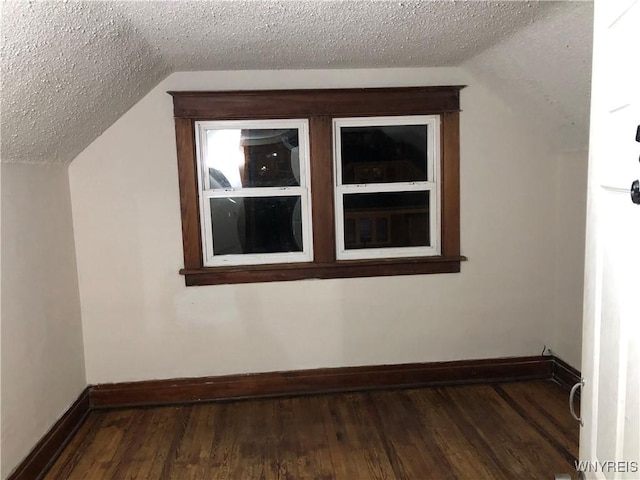 additional living space with a textured ceiling, baseboards, vaulted ceiling, and dark wood-style flooring