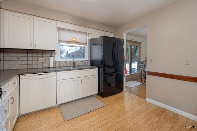 kitchen featuring dark countertops, freestanding refrigerator, white cabinetry, a sink, and dishwasher