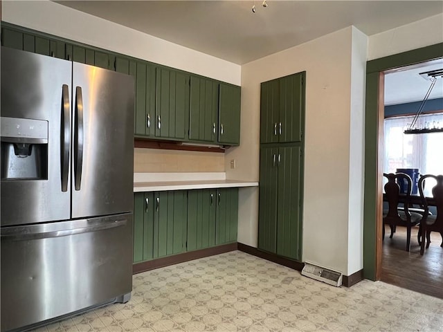 kitchen with stainless steel refrigerator with ice dispenser, light floors, light countertops, green cabinetry, and baseboards