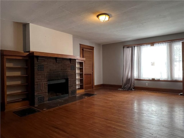 unfurnished living room featuring a brick fireplace, baseboards, and wood finished floors