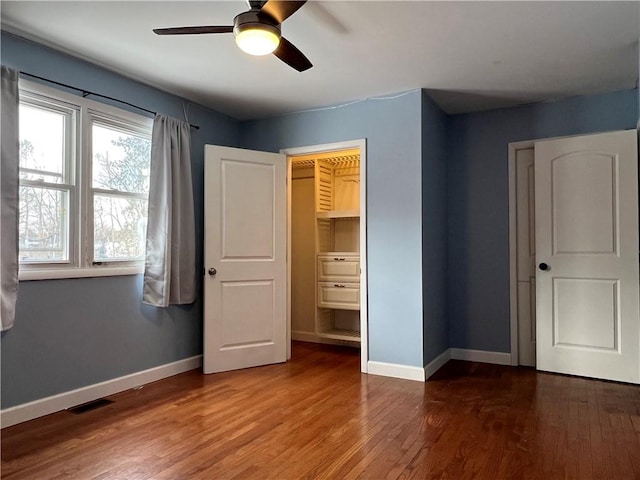 unfurnished bedroom featuring a ceiling fan, visible vents, baseboards, and wood finished floors