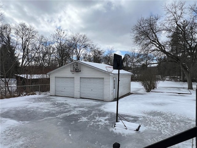 snow covered garage featuring a detached garage and fence