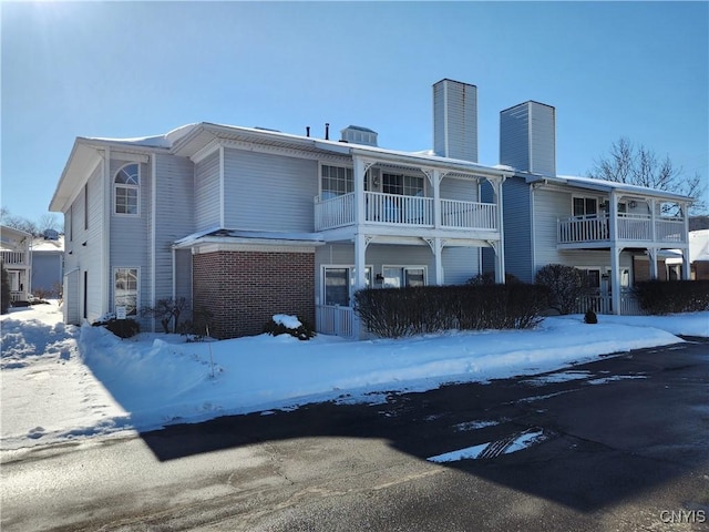 snow covered back of property with a balcony, a chimney, and brick siding