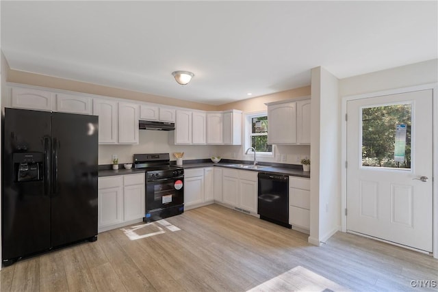 kitchen featuring light wood finished floors, dark countertops, a sink, under cabinet range hood, and black appliances