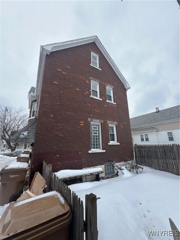 view of snowy exterior with brick siding and fence