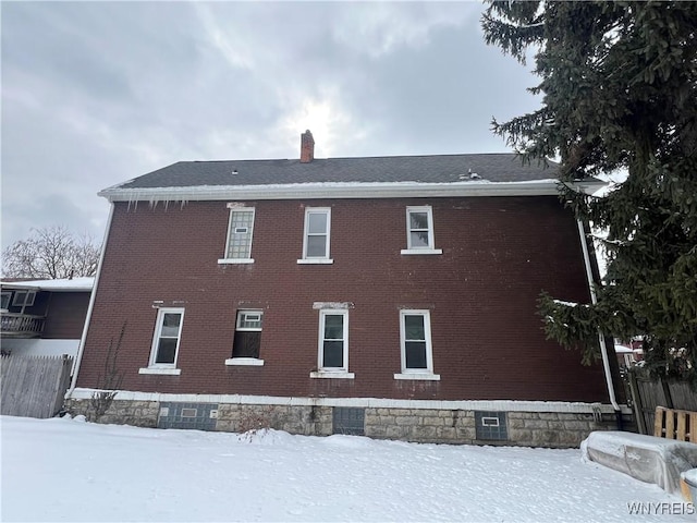 view of snowy exterior with brick siding, fence, and a chimney