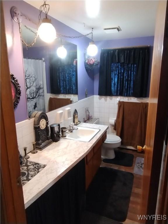 full bathroom featuring visible vents, vanity, toilet, and tile walls