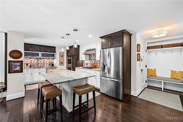 kitchen with a center island, pendant lighting, appliances with stainless steel finishes, dark brown cabinetry, and a kitchen bar