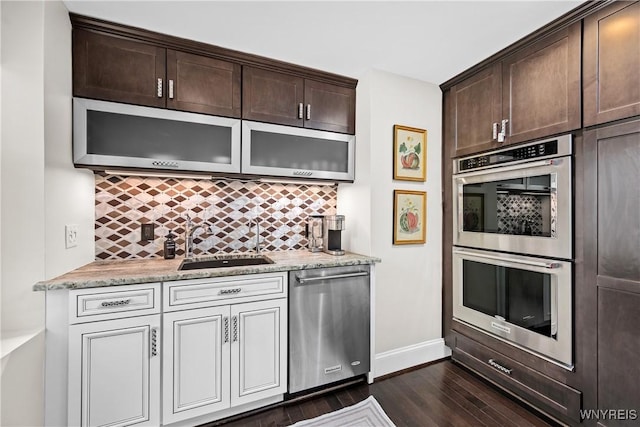 kitchen with stainless steel appliances, backsplash, a sink, and light stone countertops