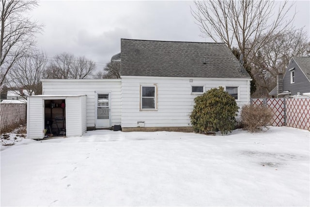 snow covered rear of property featuring roof with shingles and fence