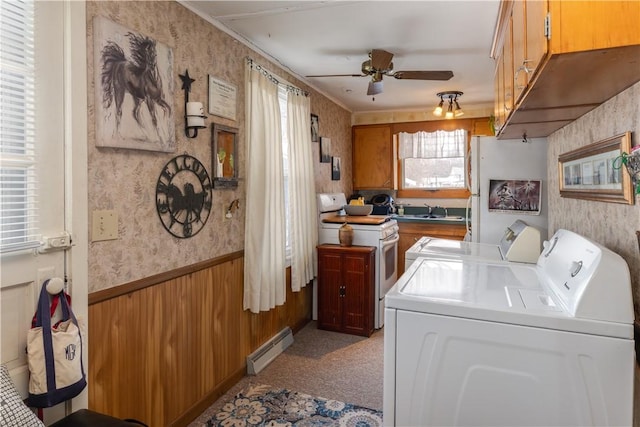 washroom with wallpapered walls, a wainscoted wall, baseboard heating, separate washer and dryer, and a sink