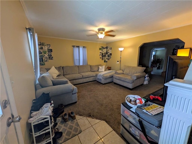 living area featuring carpet floors, arched walkways, crown molding, ceiling fan, and tile patterned floors