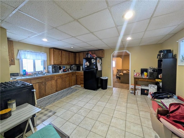 kitchen with arched walkways, a paneled ceiling, brown cabinetry, freestanding refrigerator, and stainless steel microwave