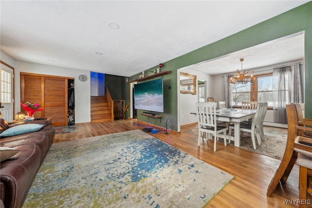 living room with baseboards, stairway, wood finished floors, an inviting chandelier, and a baseboard heating unit