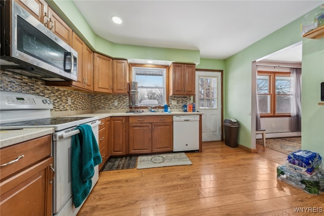 kitchen featuring a baseboard heating unit, white appliances, light countertops, light wood-type flooring, and backsplash