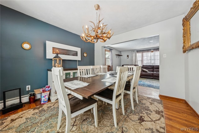 dining space with a chandelier, a baseboard radiator, baseboards, and wood finished floors