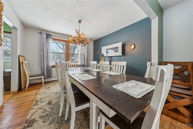 dining space with a baseboard heating unit, light wood-type flooring, and a notable chandelier