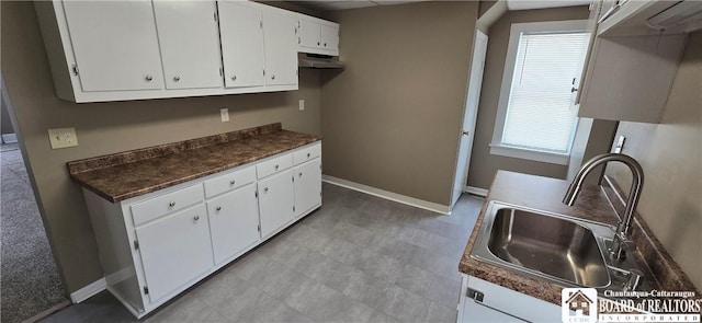 kitchen with baseboards, dark countertops, light floors, white cabinetry, and a sink