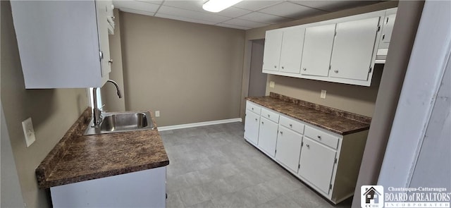 kitchen with a drop ceiling, dark countertops, light floors, white cabinetry, and a sink