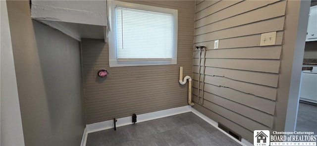 laundry area featuring dark floors, wood walls, visible vents, and baseboards