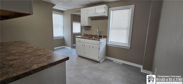 kitchen with dark countertops, white cabinets, a sink, and baseboards