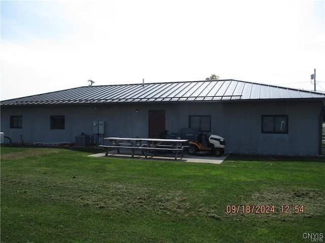 back of property with a standing seam roof, a lawn, metal roof, and central AC