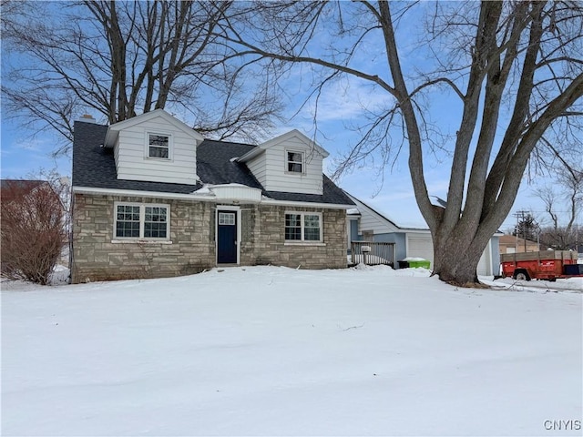 new england style home with stone siding, a shingled roof, and a chimney