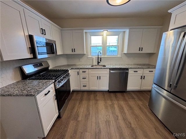 kitchen with appliances with stainless steel finishes, white cabinets, a sink, and light stone countertops