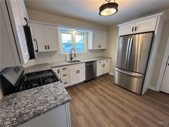 kitchen with light stone counters, stainless steel appliances, dark wood-type flooring, white cabinets, and a sink