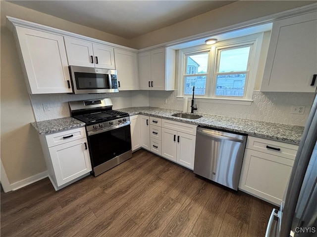 kitchen featuring light stone counters, stainless steel appliances, a sink, white cabinets, and dark wood finished floors