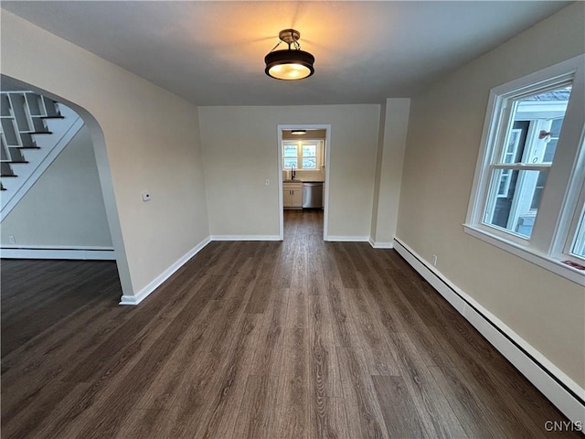 unfurnished dining area with a baseboard heating unit, arched walkways, baseboards, and dark wood-style floors