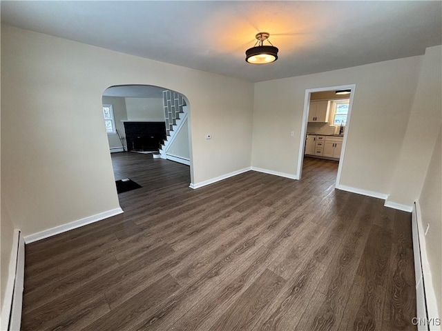 spare room featuring dark wood-style floors, a baseboard radiator, arched walkways, and baseboards