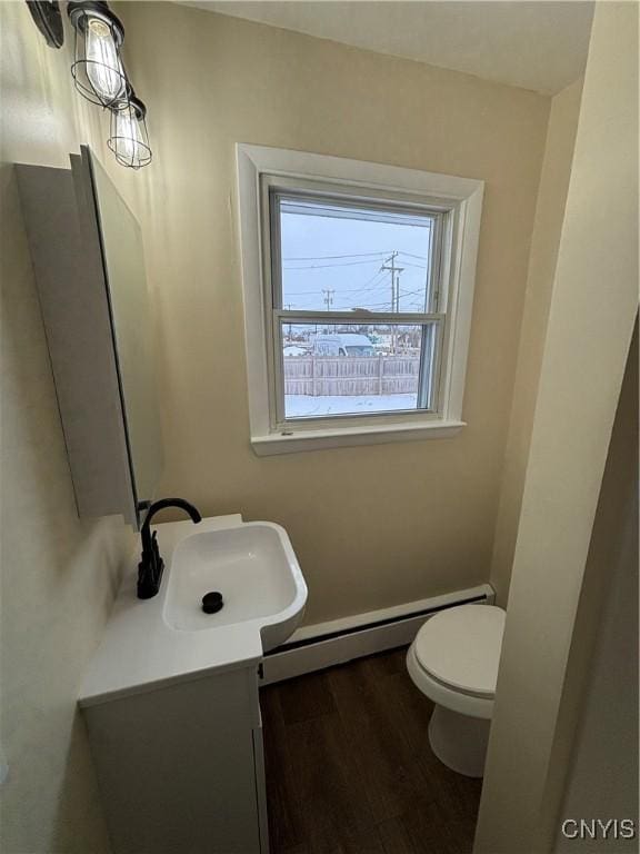 half bath with toilet, baseboard heating, wood finished floors, and vanity