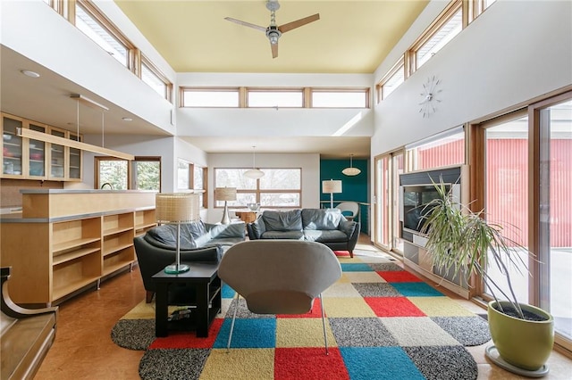 living area with a fireplace, a towering ceiling, a wealth of natural light, and a ceiling fan